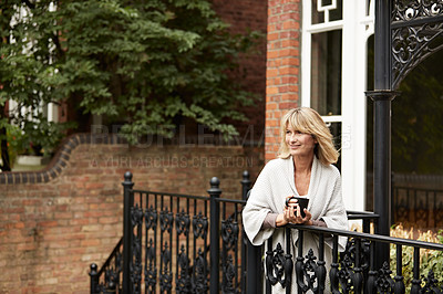 Buy stock photo Shot of a mature woman standing on her front porch drinking a cup of coffee