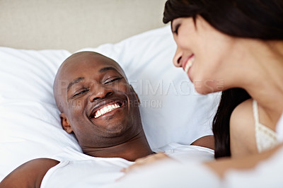 Buy stock photo Shot of a young couple laughing while lying in bed together