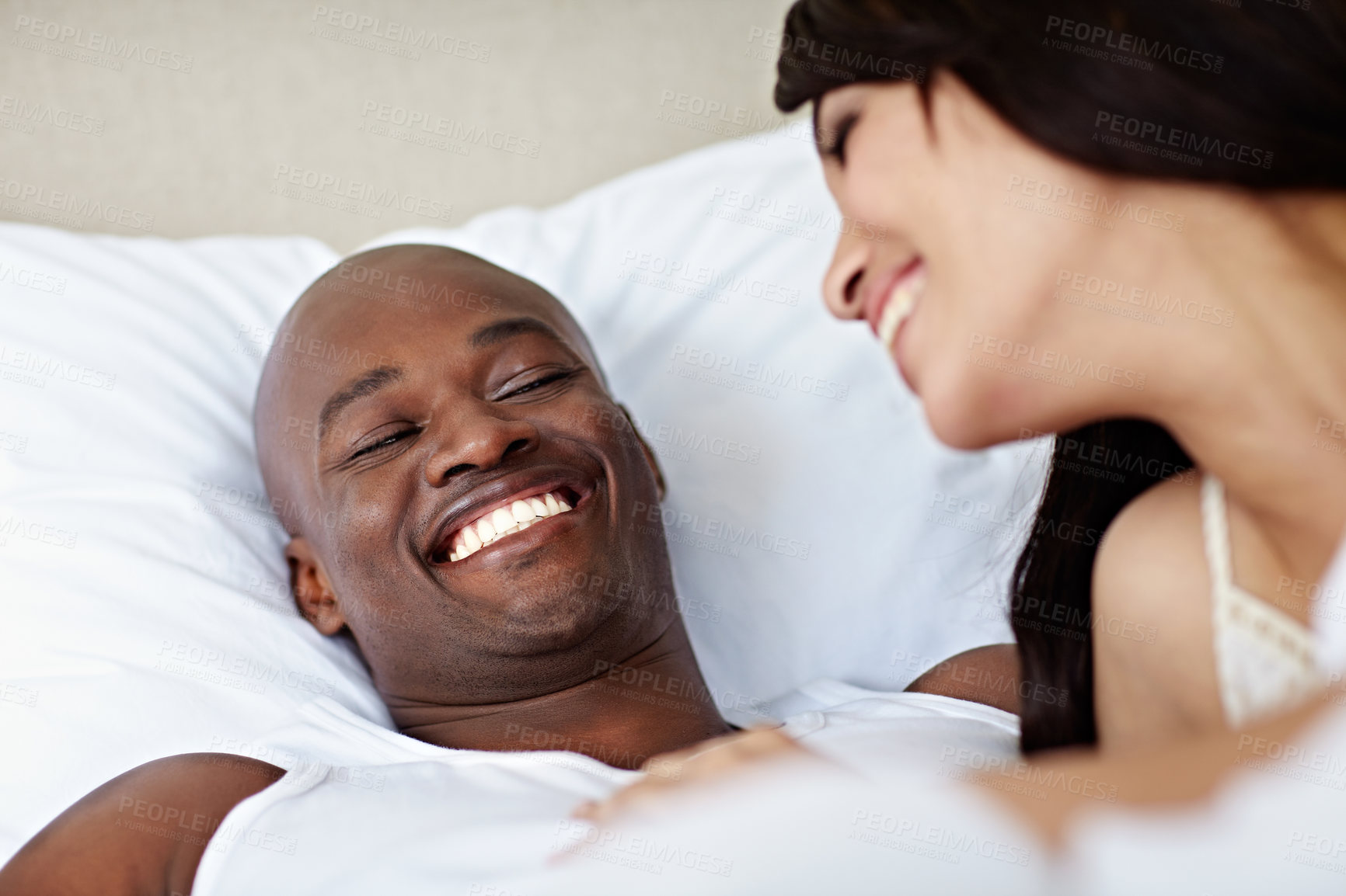 Buy stock photo Shot of a young couple laughing while lying in bed together