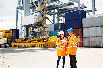 Buy stock photo Shot of two dock workers looking through paperwork while standing in a dockyard