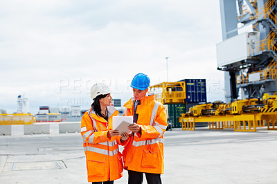 Buy stock photo Shot of two dock workers looking through paperwork while standing in a dockyard