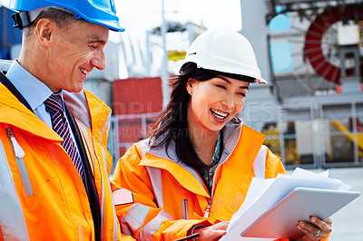 Buy stock photo Shot of two dock workers looking through paperwork while standing in a dockyard