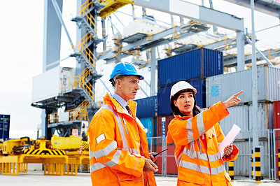 Buy stock photo Shot of two dock workers talking together while standing in a dockyard