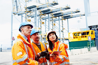 Buy stock photo Shot of three workers talking together over a digital tablet while standing on a commercial dock