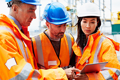 Buy stock photo Shot of three workers talking together over a digital tablet while standing on a commercial dock