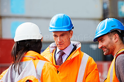 Buy stock photo Shot of three workers talking together while standing on a commercial dock