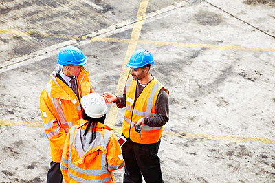 Buy stock photo Shot of three workers talking together while standing on a commercial dock
