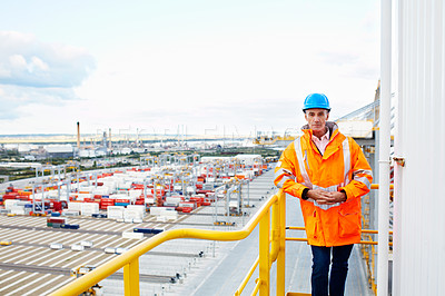 Buy stock photo Portrait of a man in workwear standing on a walkway looking out over at a large commercial dock