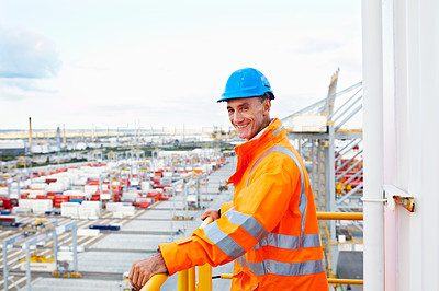 Buy stock photo Portrait of a man in workwear standing on a walkway looking  out over at a large commercial dock