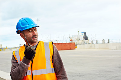 Buy stock photo Shot of a young man in workwear talking on a walkietalkie while standing on a large commercial dock