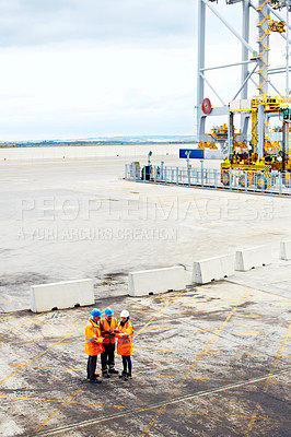 Buy stock photo High angle shot of three workers talking together while standing on a commercial dock