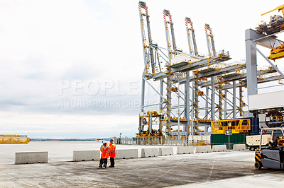 Buy stock photo Shot of three workers talking together while standing on a commercial dock