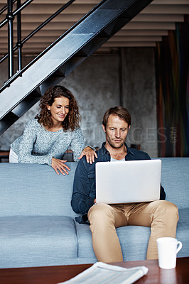 Buy stock photo Shot of a man sitting on the sofa using a laptop with his wife looking over his shoulder