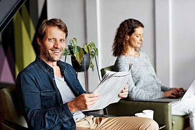Buy stock photo Portrait of a mature couple sitting in their living room reading the newspaper and using a laptop