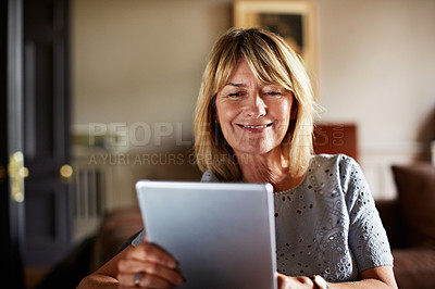 Buy stock photo Shot of a mature woman sitting on her sofa using a digital tablet
