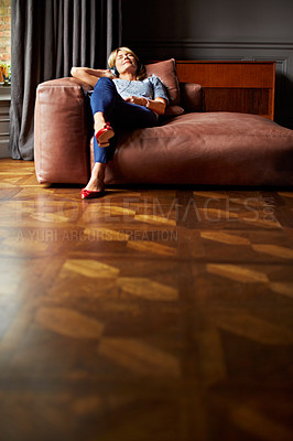 Buy stock photo Shot of a mature woman lying back on her sofa listening to music on headphones