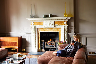 Buy stock photo Shot of a mature woman relaxing on her living room sofa with a fire glowing in the background