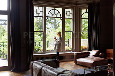 Buy stock photo Shot of a mature woman drinking tea while looking out of her living room window