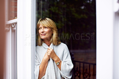 Buy stock photo Shot of a mature woman clutching her sweater while looking out of her living room window