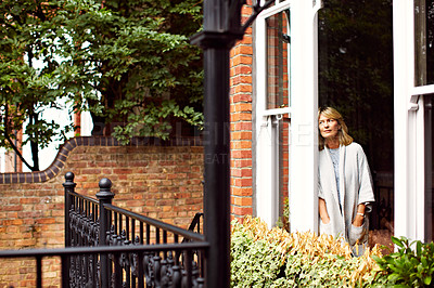 Buy stock photo Shot of a mature woman looking out of her living room window