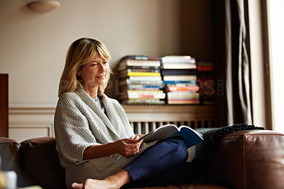 Buy stock photo Shot of a mature woman reading a book while sitting on her sofa