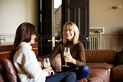 Buy stock photo Shot of two women sitting on a sofa drinking wine and talking