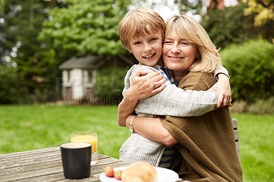 Buy stock photo Portrait of a grandmother and her grandson hugging while sitting at a table in her yard