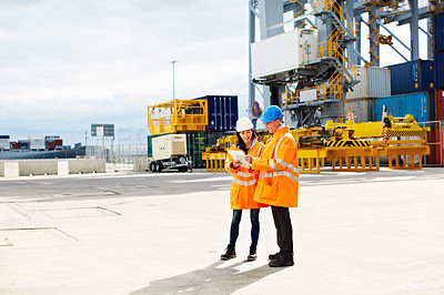 Buy stock photo Shot of two dock workers looking through paperwork while standing in a dockyard