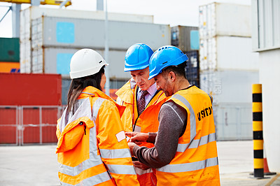 Buy stock photo Shot of three workers talking together over a digital tablet while standing on a commercial dock