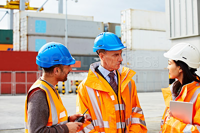 Buy stock photo Shot of three workers talking together while standing on a commercial dock