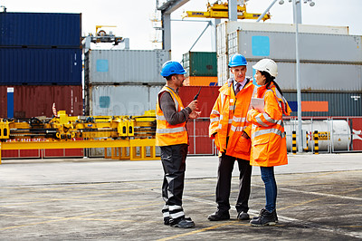 Buy stock photo Shot of three workers talking together while standing on a commercial dock