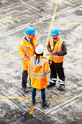 Buy stock photo High angle shot of three workers talking together while standing on a commercial dock