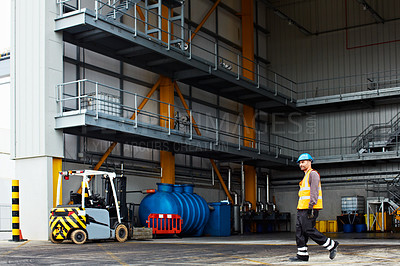 Buy stock photo Shot of a dock worker walking in front of a large warehouse on a commercial dock