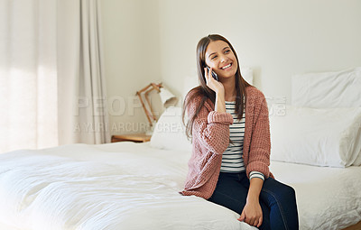 Buy stock photo Shot of a young woman sitting on her bed talking on a cellphone
