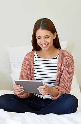 Buy stock photo Shot of a young woman sitting on her bed using a digital tablet