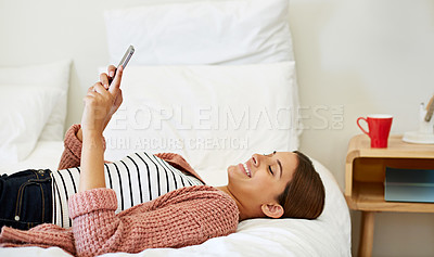 Buy stock photo Shot of a young woman lying on her bed using a cellphone