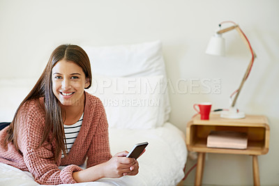 Buy stock photo Portrait of a young woman lying on her bed using a cellphone