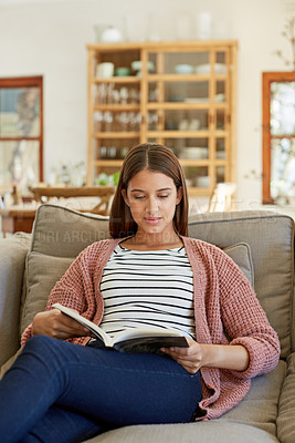 Buy stock photo Shot of a young woman sitting on her sofa reading a book