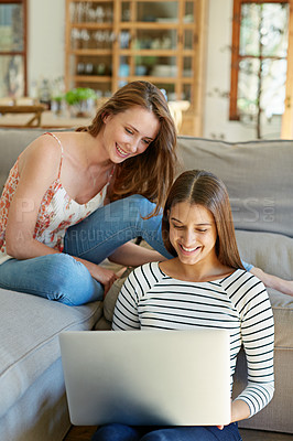 Buy stock photo Shot of two young friends sitting in the living room using a laptop together