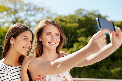 Buy stock photo Shot of two friends taking a selfie together while standing outside