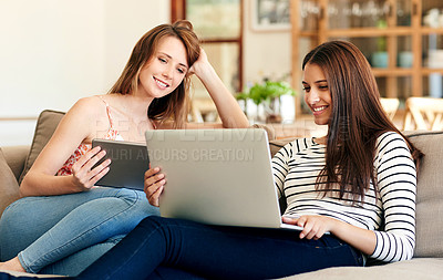 Buy stock photo Shot of two young friends sitting on the sofa using a laptop and digital tablet