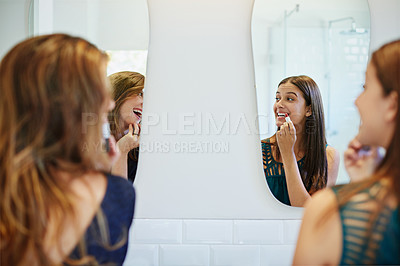 Buy stock photo Shot of two young friends putting on makeup in the bathroom mirror