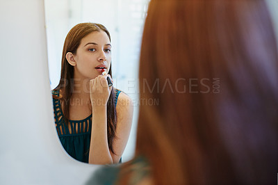 Buy stock photo Shot of a young woman putting on lipstick in her bathroom mirror