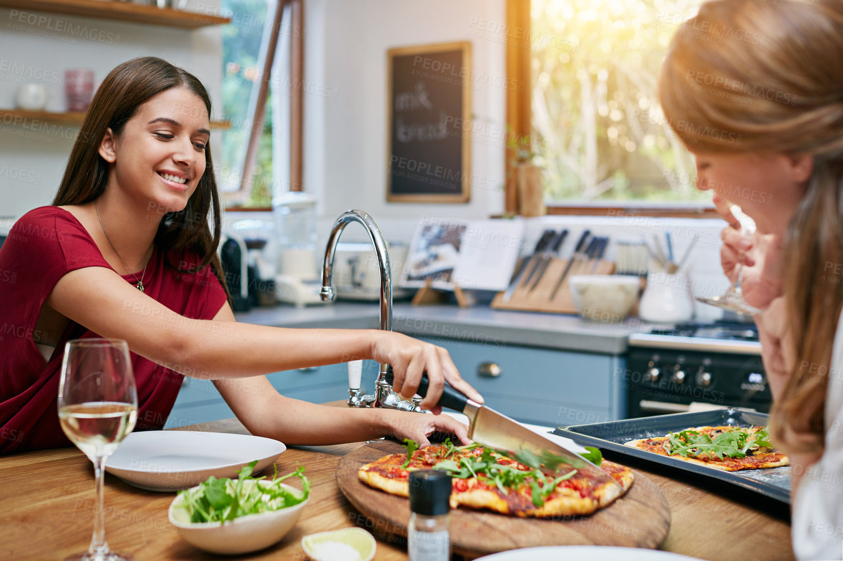 Buy stock photo Shot of two friends sitting at the kitchen table eating pizza and drinking wine