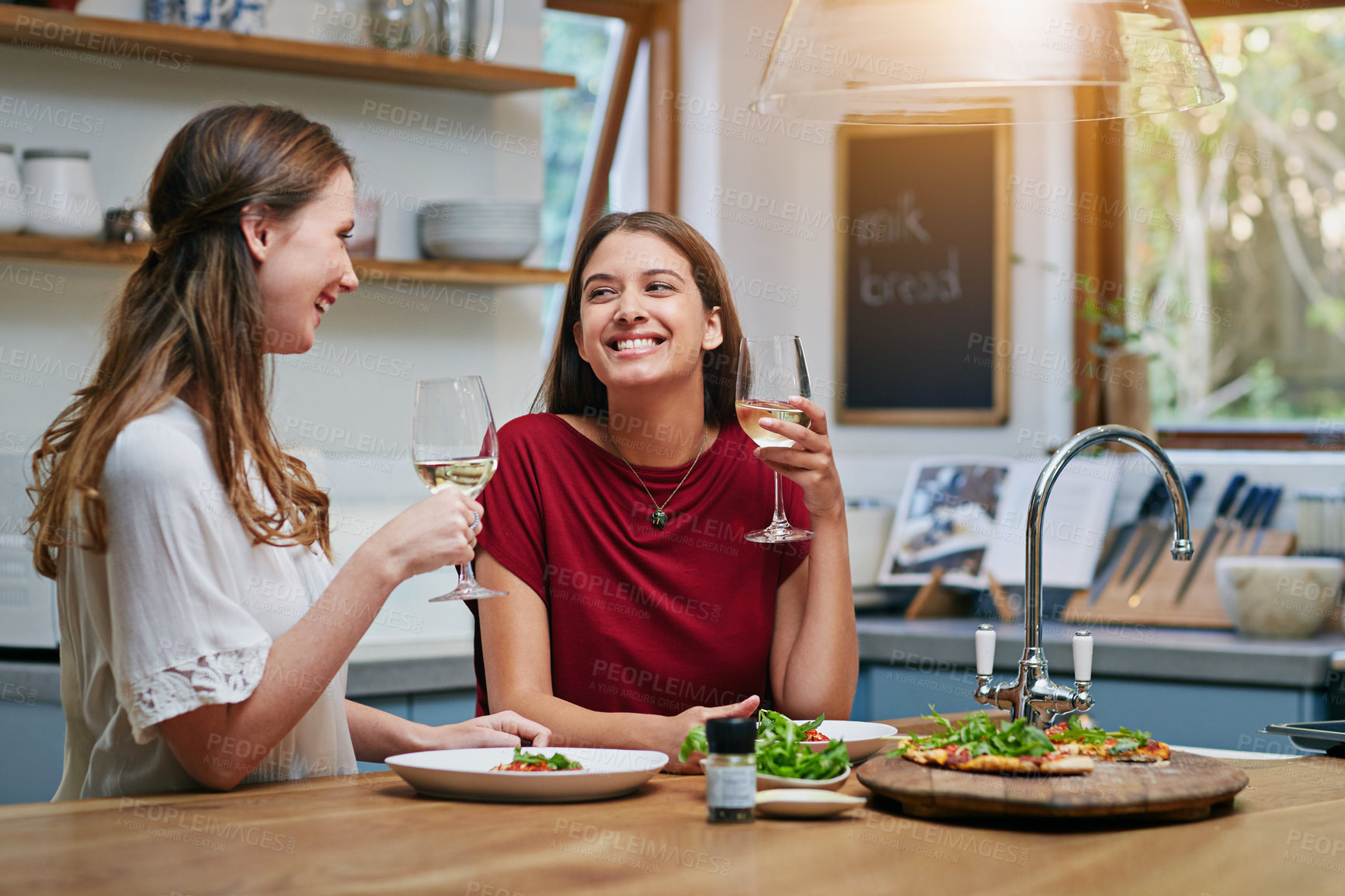 Buy stock photo Women, laugh and pizza in kitchen with wine, relax and happy with lunch for bonding in home. People, friends and smile with alcohol, food and conversation with snack for support or relationship