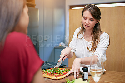 Buy stock photo Shot of two friends sitting at the kitchen table eating pizza and drinking wine