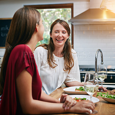 Buy stock photo Shot of two friends sitting at the kitchen table eating pizza and drinking wine