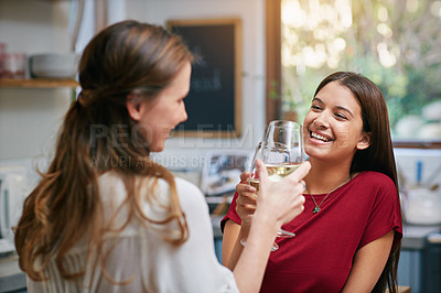 Buy stock photo Shot of two friends standing in a kitchen drinking wine together