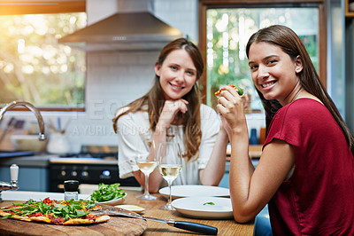 Buy stock photo Portrait of two friends sitting at the kitchen table eating pizza and drinking wine