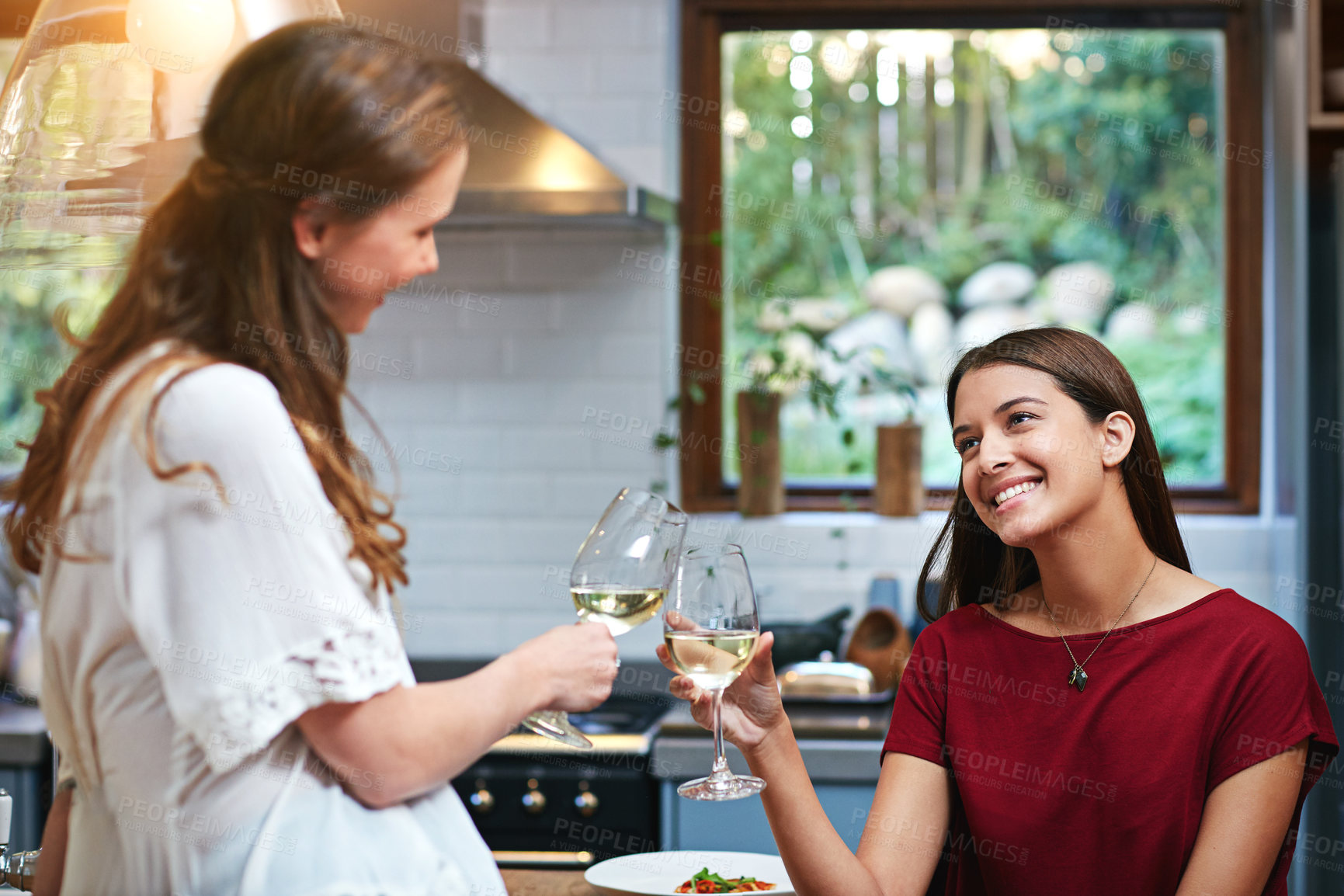 Buy stock photo Shot of two friends standing in a kitchen drinking wine together